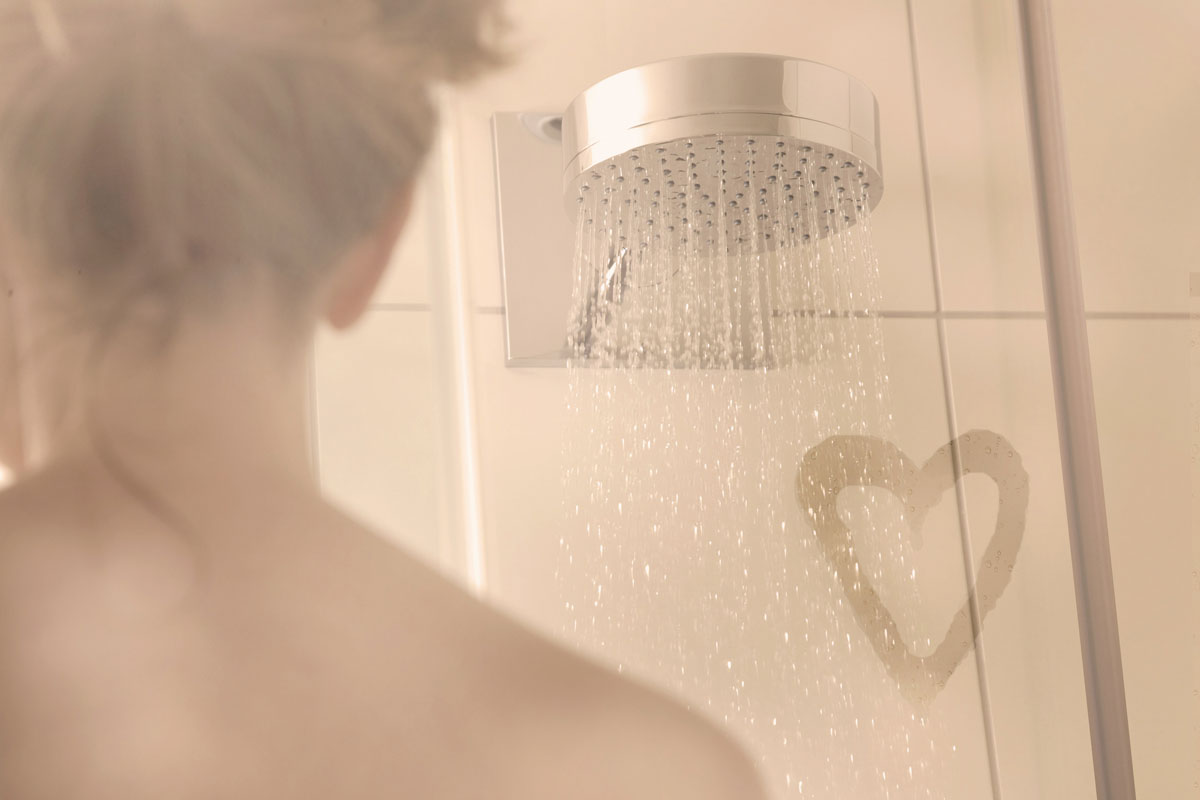 Woman takes a shower, with a love heart in the steam of the shower screen