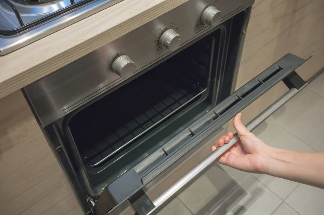 Woman's Hands open the black and silver door of oven machine for cooking