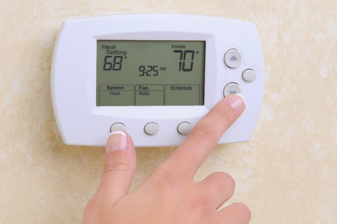 Woman's hand setting the room temperature on a modern programmable thermostat
