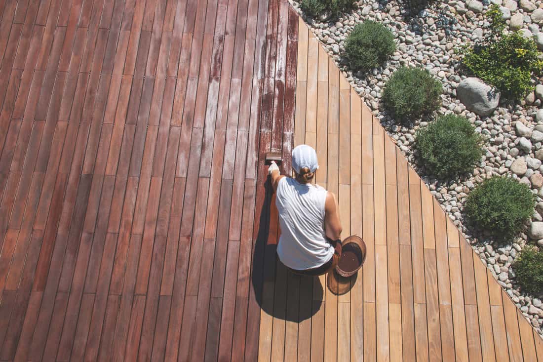 Wood deck renovation treatment,the person applying protective wood stain with a brush, overhead-view of- ipe hardwood decking restoration process