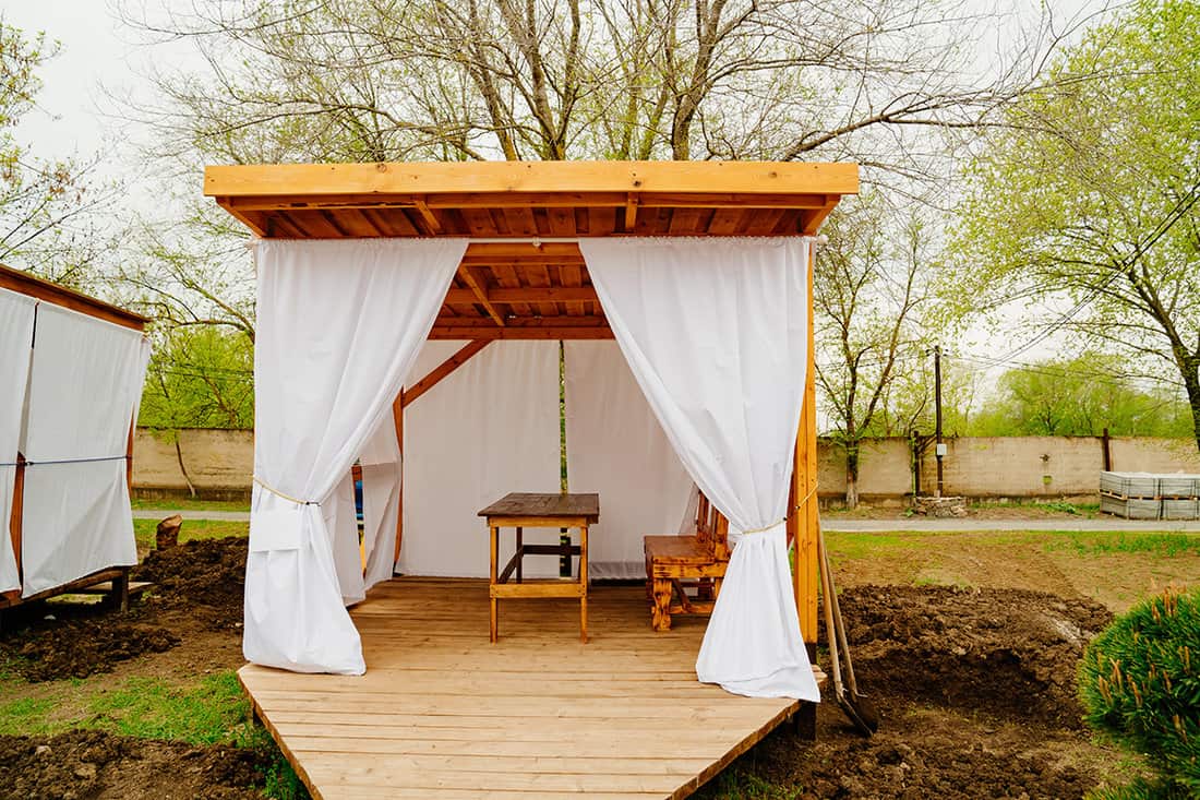 Wooden gazebo with white curtains for lunch in nature