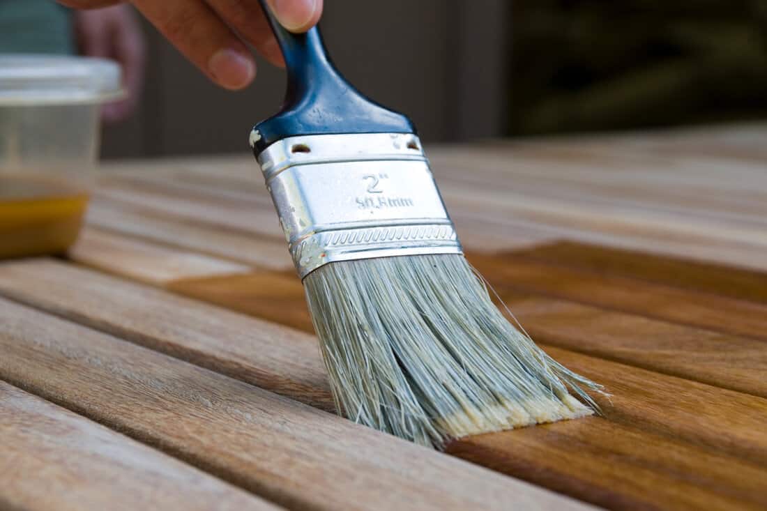 applying a coat of teak oil to the surface of a patio table top