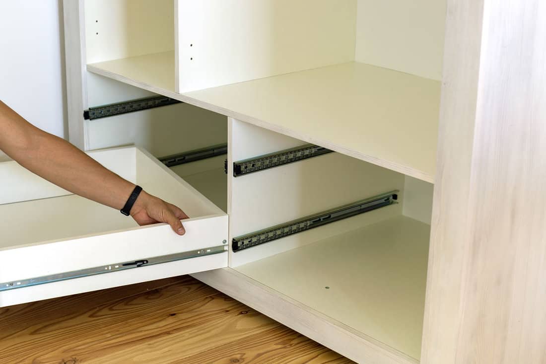 carpenter hands installing wooden drawer on sliding skids in contemporary cupboard cabinet