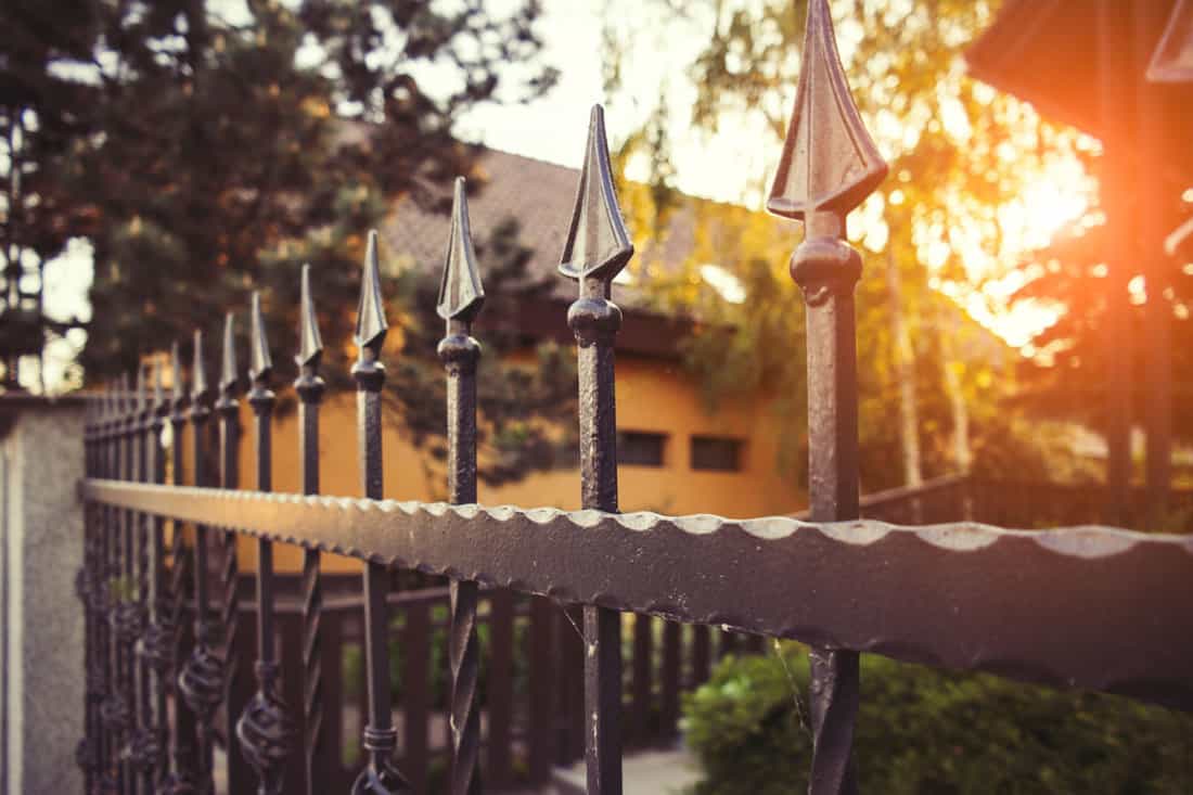 close up photo of a black classic metal gate outside the mansion, sun lit photo, sun set photo