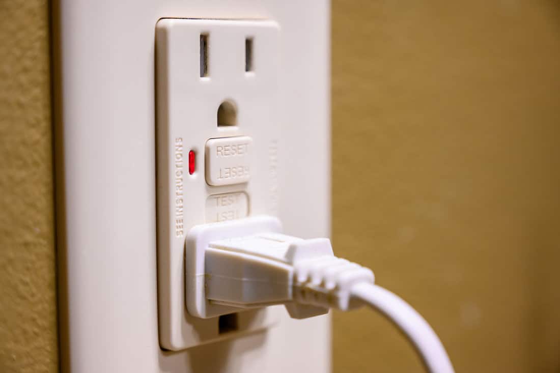 close up photo of an electrical outlet, white plug on it, brown painted wall