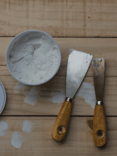 different size putty knives and a tub of wood filler on a table top. How To Mix And Use Bondo Wood Filler
