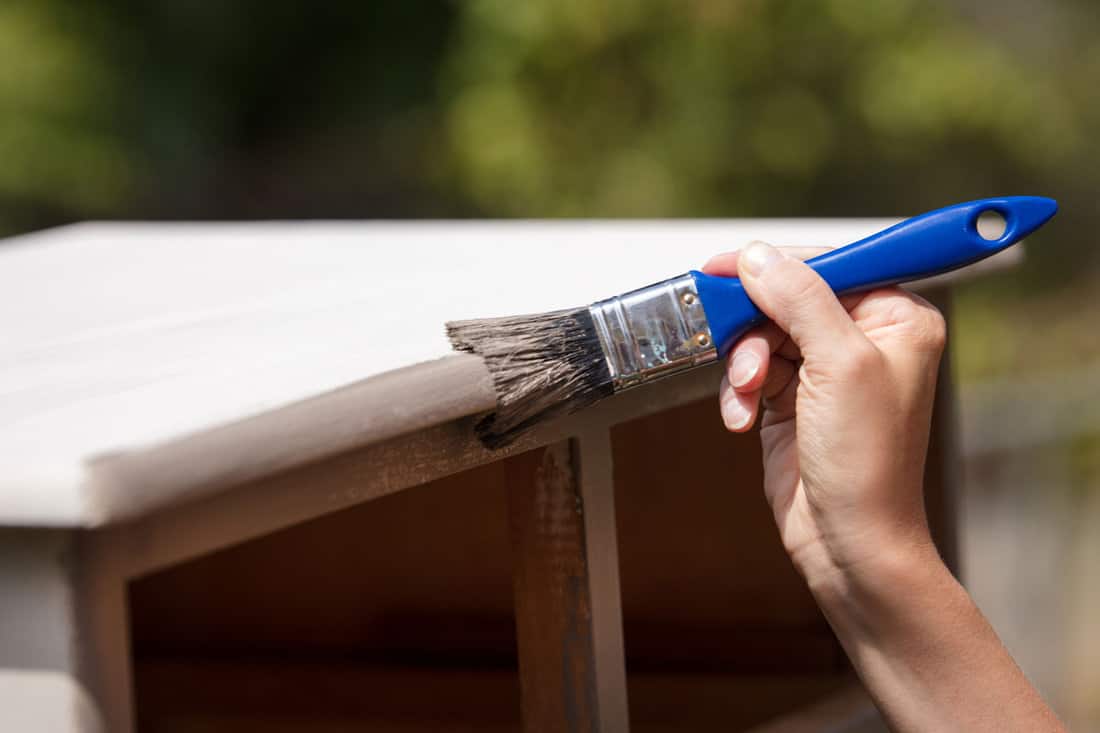 man hand holding a blue paint brush, painting a wood closet on the outside of the house