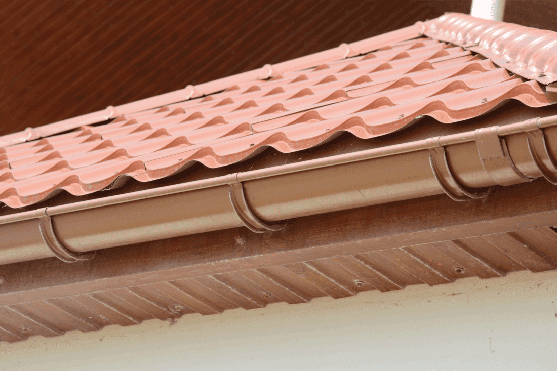 red metal tile rooftop with wood soffit, house eaves, rafters and installed rain gutter.