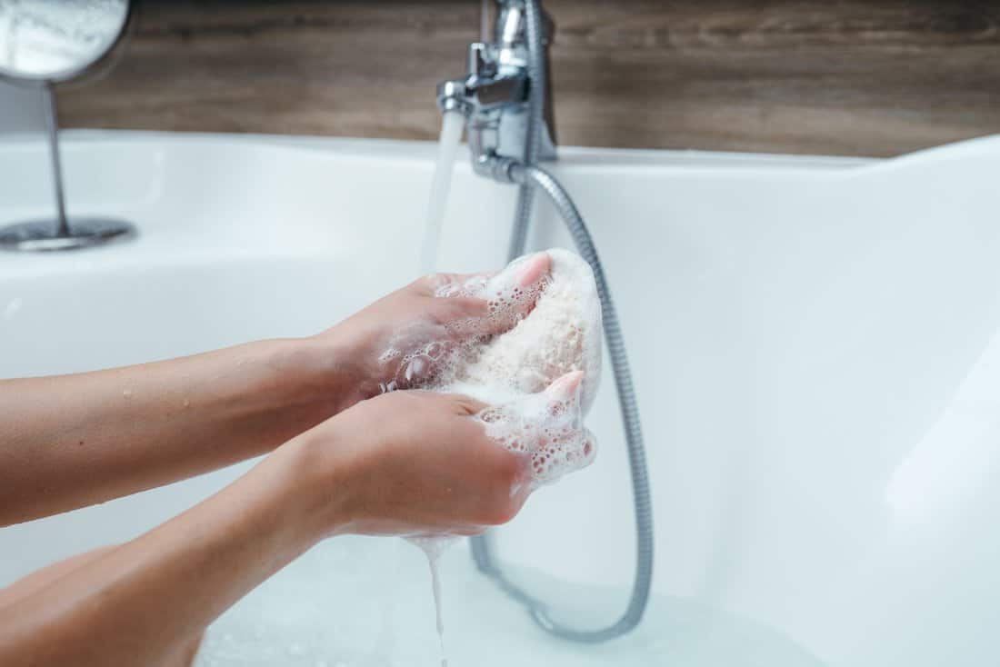 Close-up of female hands with a washcloth. Woman foaming a washcloth with gel for Lush while sitting in a bath