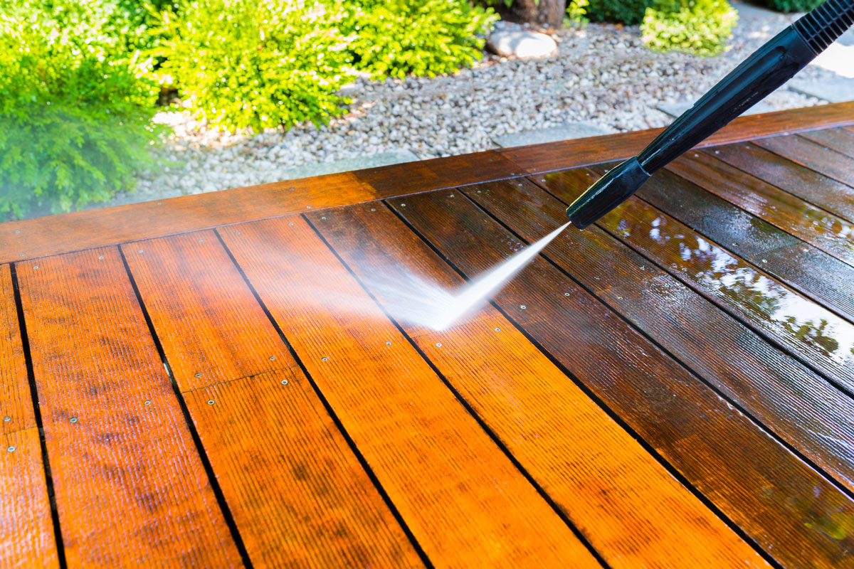 washing wood deck using pressure washer on a sunny day