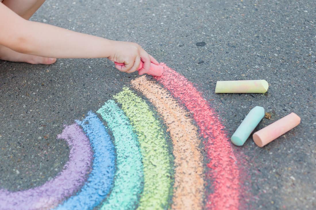 woman hands holding a huge red chalk, drawing a rainbow on the concrete ground, colorful chalks