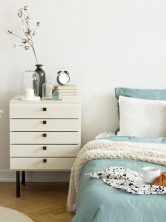 A bright bedroom interior with sage green and white bedding, pillows on bed and a drawer nightstand. - Can You Spray Paint A Nightstand [And How To]