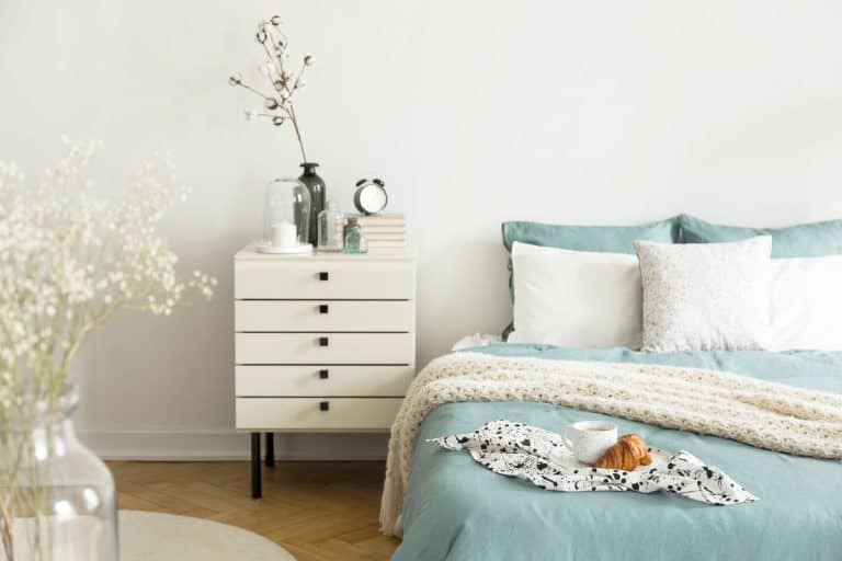 A bright bedroom interior with sage green and white bedding, pillows on bed and a drawer nightstand. - Can You Spray Paint A Nightstand [And How To]