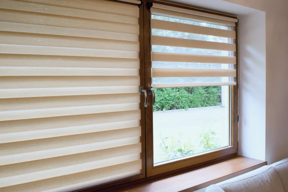 A deep beige colored window with wooden framing and blinds