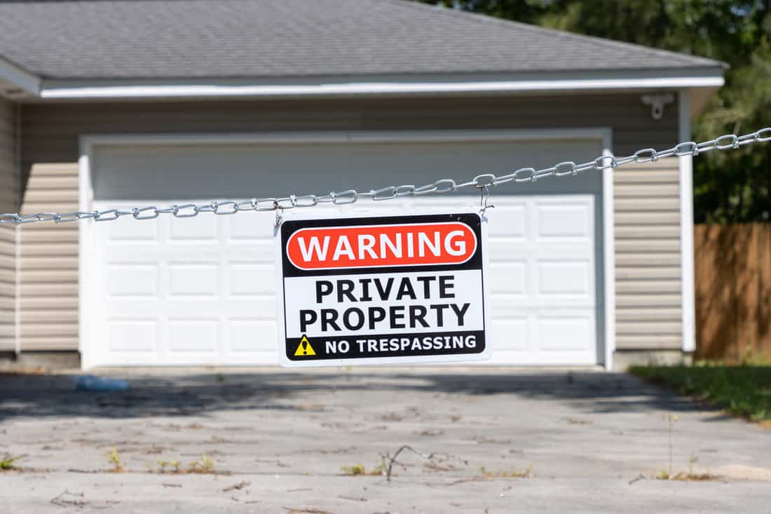 A private property no trespassing sign hangs from a chain across a driveway in front of a garage of a suburban house