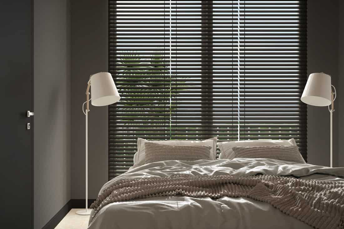 A small bedroom with brown blinds and a white study lamp