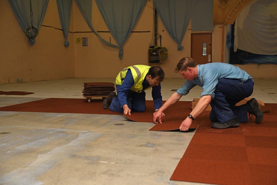 A team of tradesman lay new carpet squares in a commercial building.