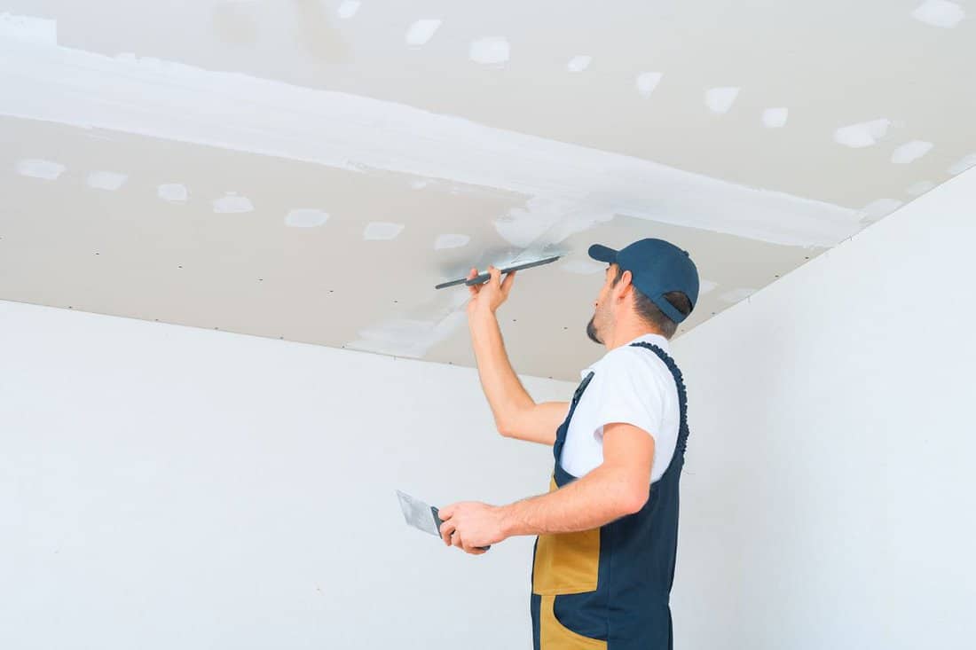 A uniformed worker applies putty to the drywall ceiling. Putty of joints of drywall sheets.