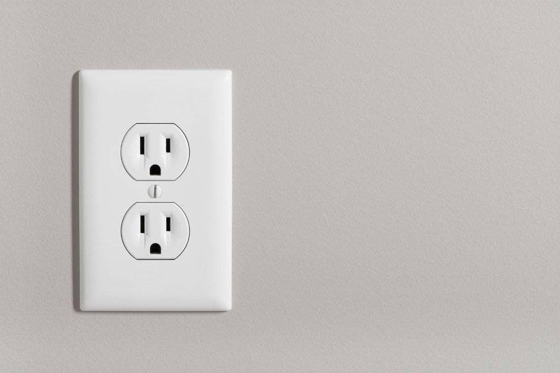 A white home electrical outlet on a light grey wall.