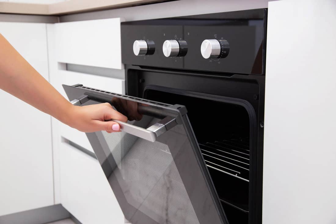 A woman's hand opens the door of an electric convection oven. Built-in oven in the kitchen