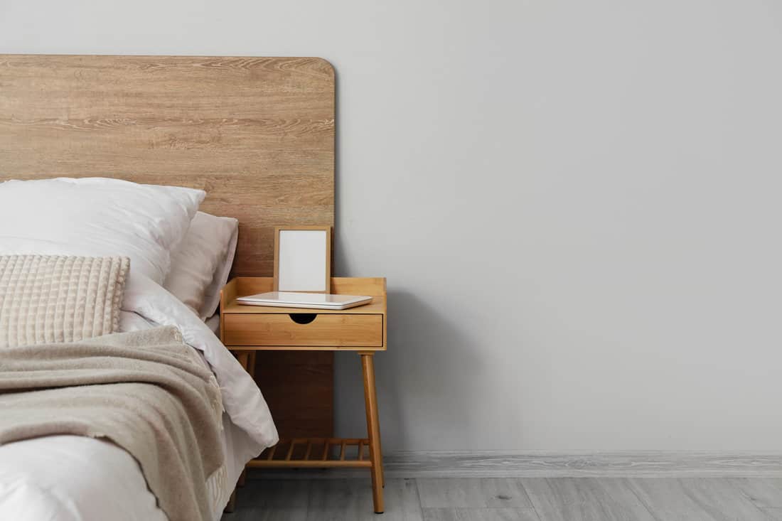 A wooden bedside table with a laptop on top and an empty picture frame