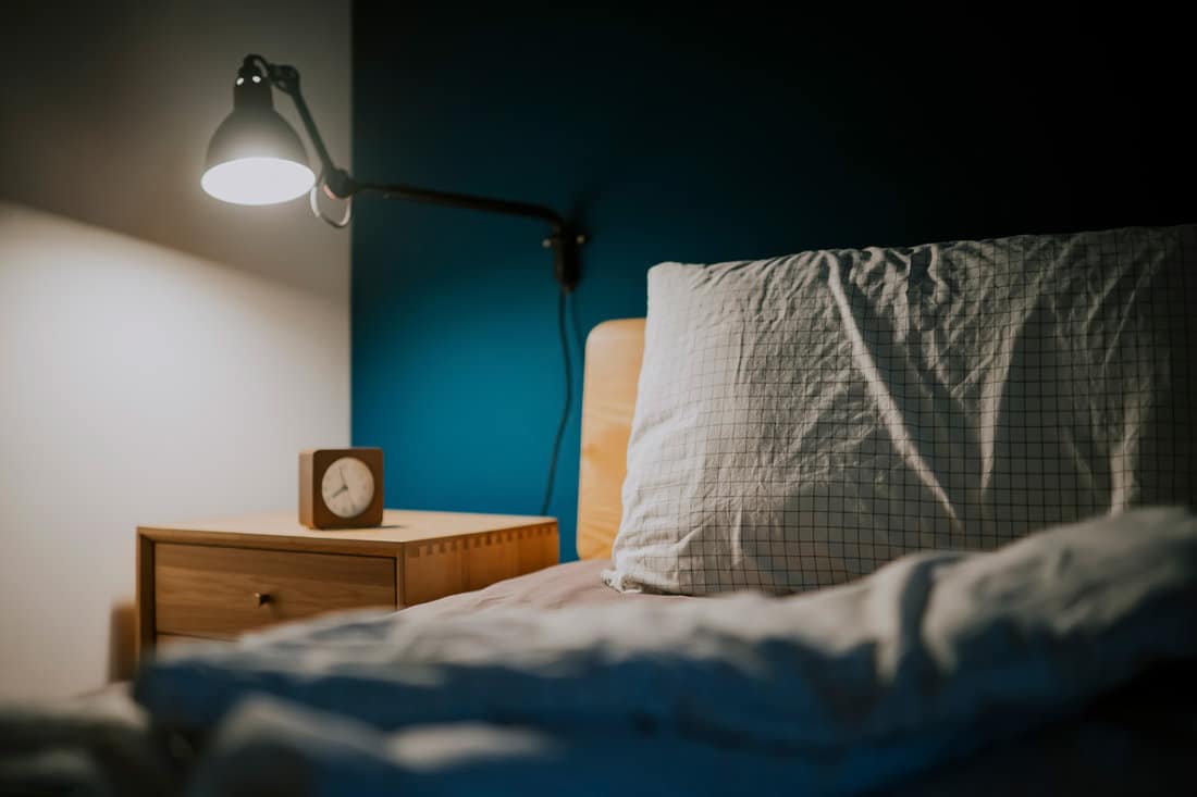 A wooden nightstand with a lamp and a clock