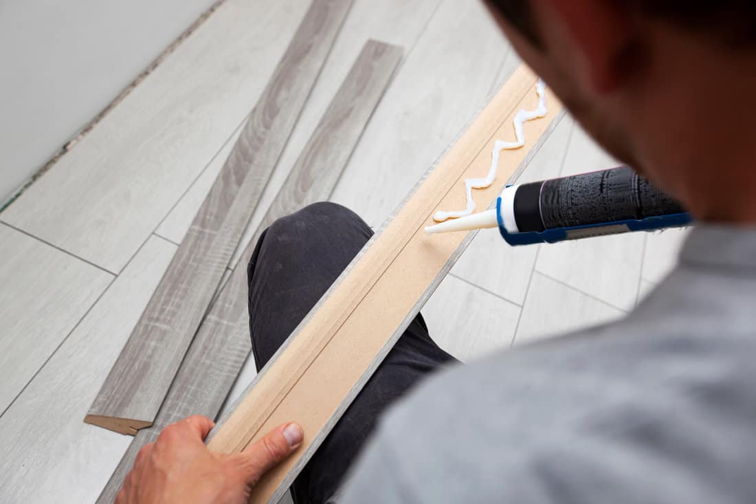 A worker applies glue to a baseboard before installing it on the floor