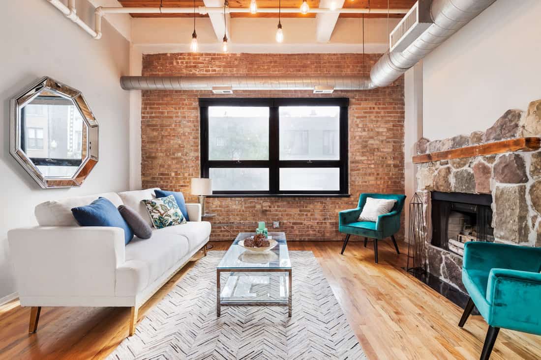 An exposed brick and wood, timber and brick, condo with furniture sitting across a large stone fireplace o