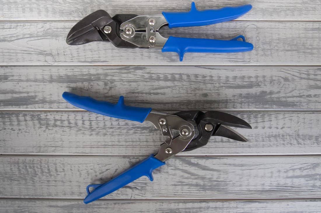 Two tin snips or metal scissors on a grey wooden background