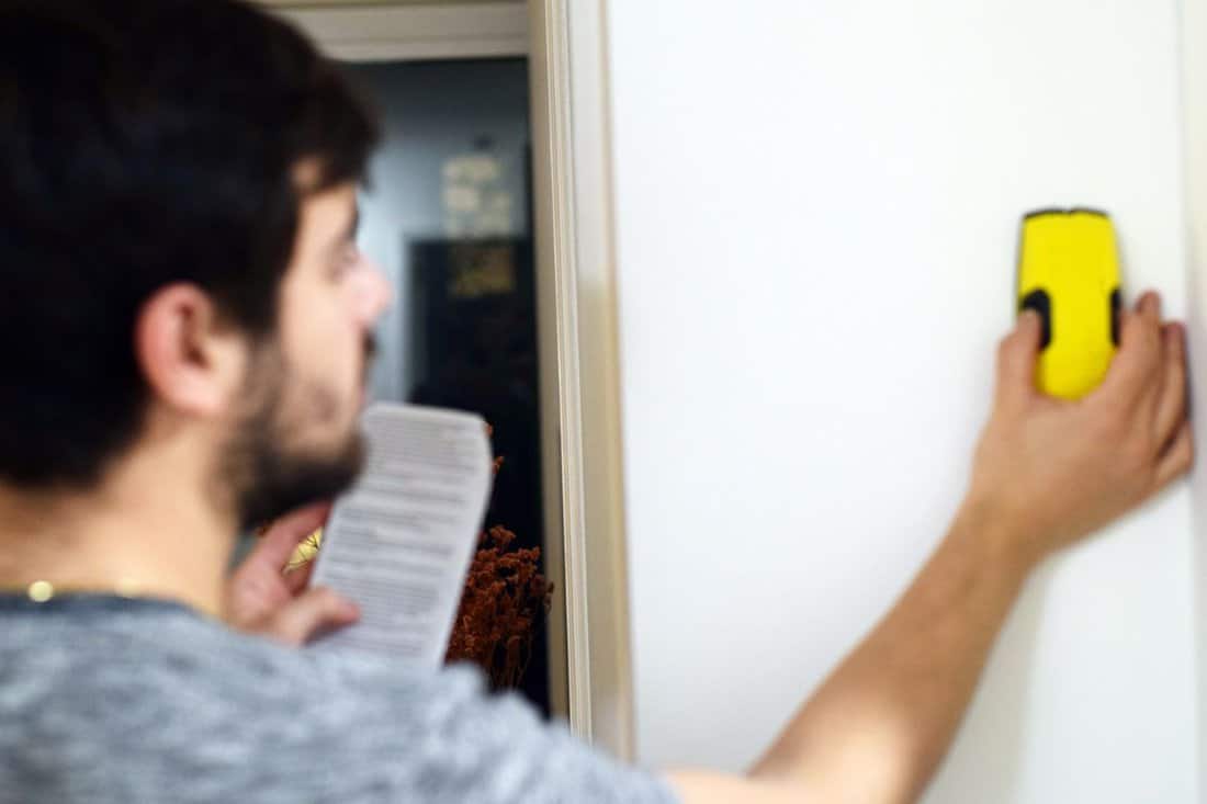 Blurred man using stud finder to search apartment wall for studs and live wires