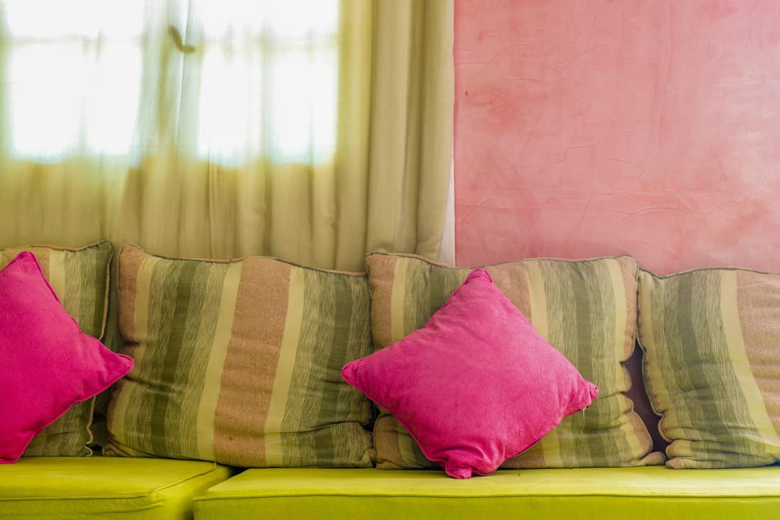 Bright colorful cushions on the sofa with light coming in from the curtain-covered window on the background
