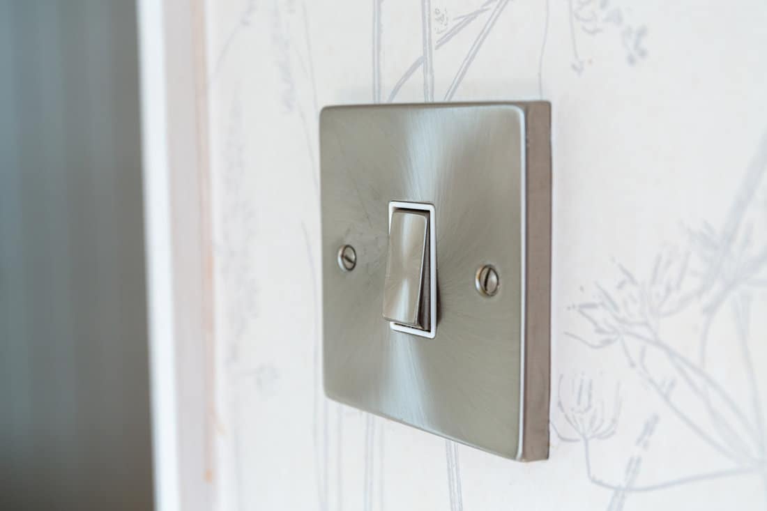 Brushed chrome light switch on a wall with patterned wallpaper