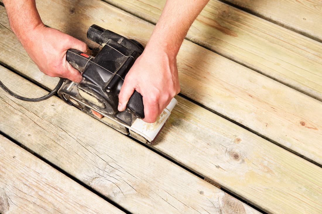 Carpentry sanding the wooden deck using a power tool
