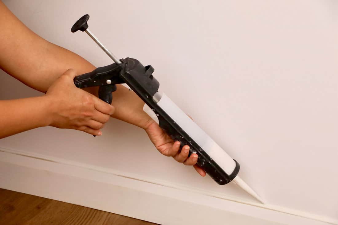 Close-up of a female contractor using a mastic gun to seal a baseboard