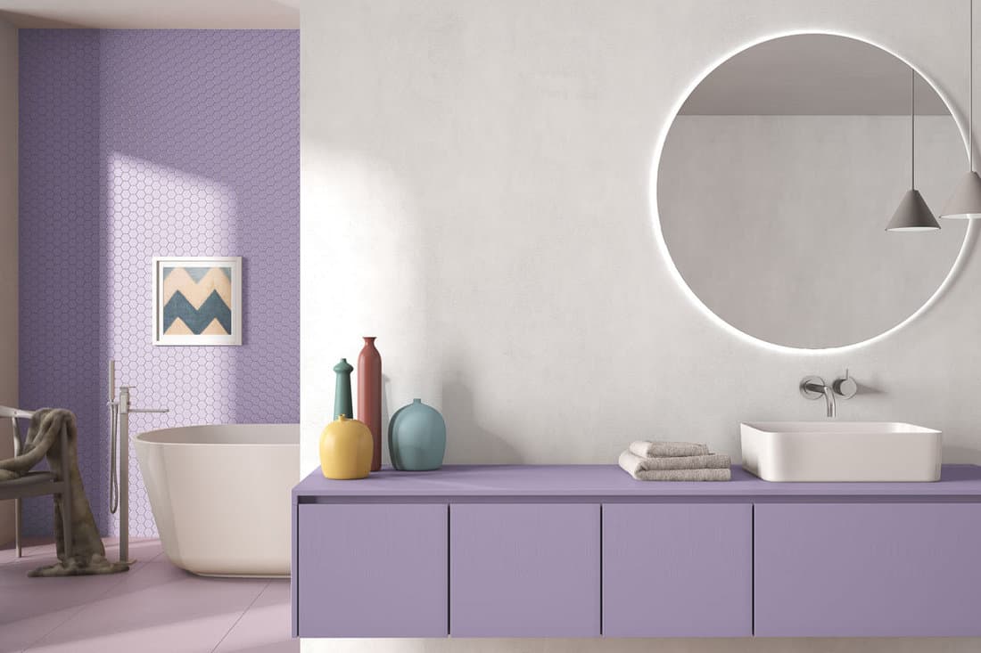 Cozy minimalist bathroom in purple pastel tones, washbasin with mirror, bathtub, tiles and concrete walls, armchair
