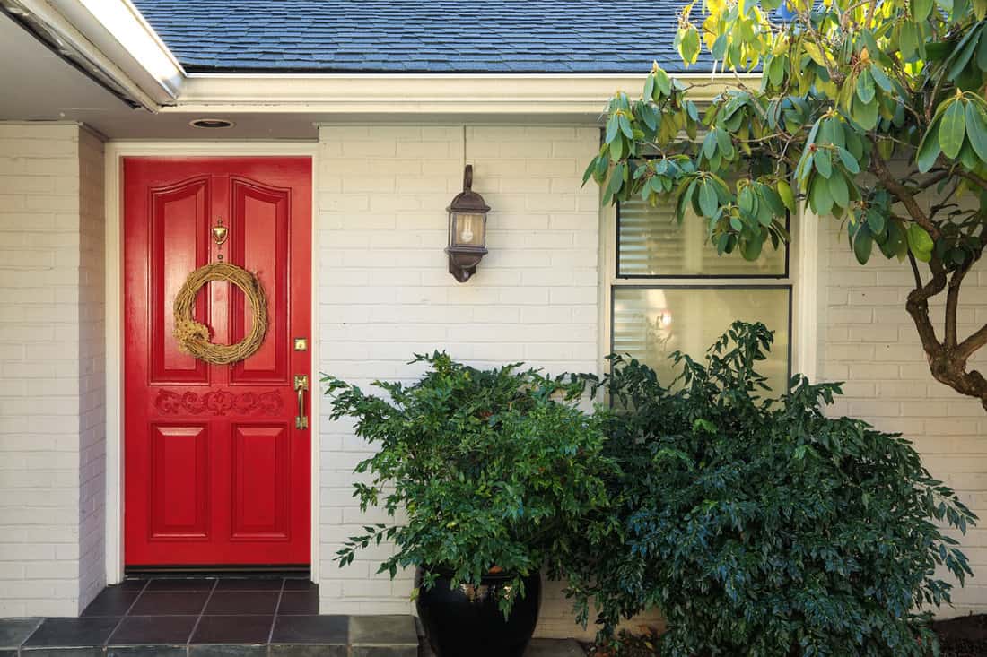Front porch with white painted brick exterior, red entrance door accented with Door Wreath and finished with pot planter under wall lantern. Northwest, USA
