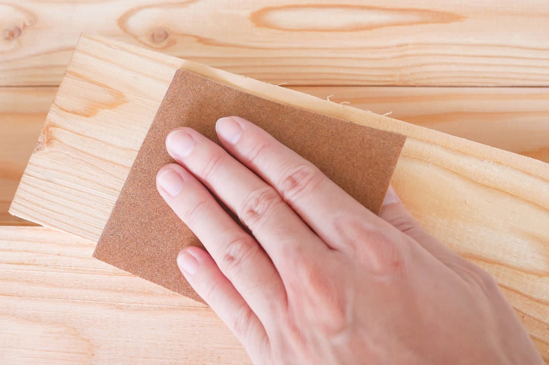 Hand sanding wooden pallet with sandpaper.