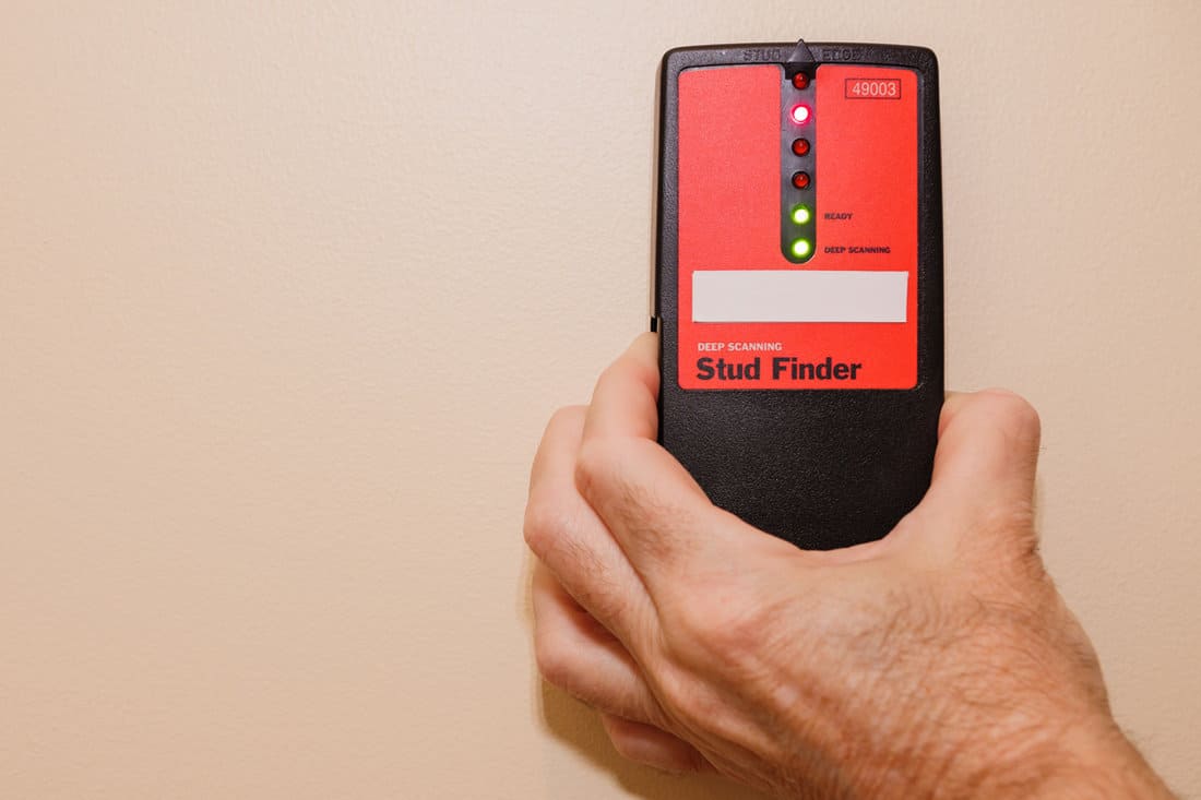 Holding a stud finder on a dry wall
