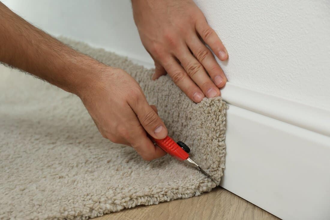 How to turn and tack carpet - Worker with cutter knife installing new carpet indoors, closeup