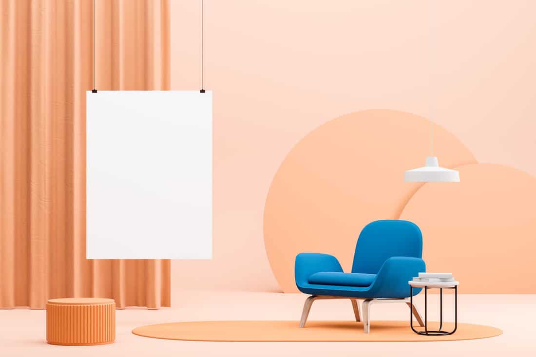 Interior of bright minimalistic living room with peach colored walls and floor, bright blue armchair on carpet, coffee table and vertical mock up poster.
