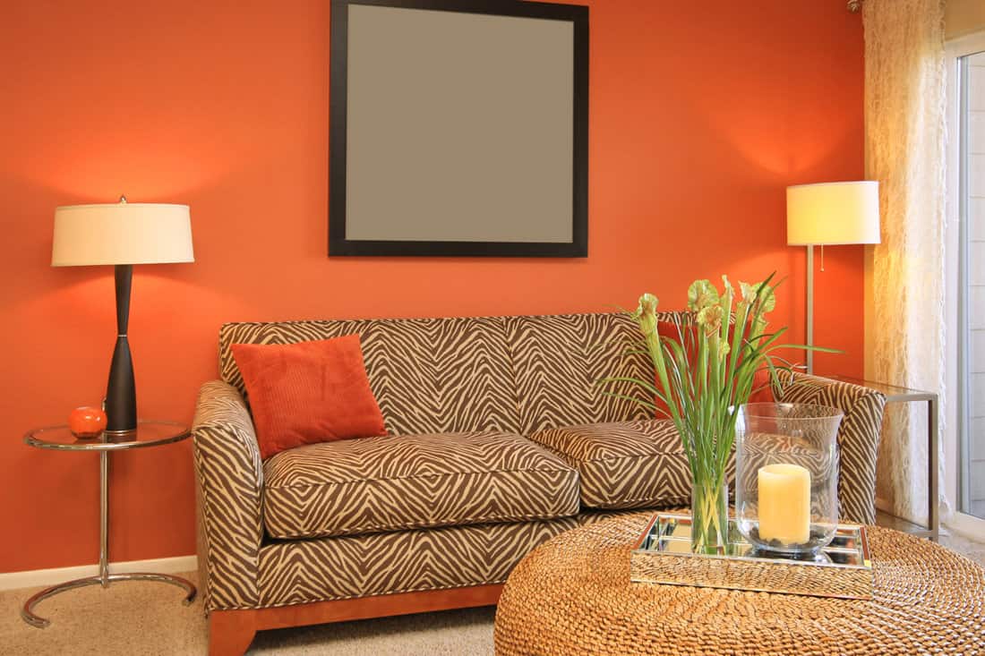 Interior of a modern orange themed living room with brown patterned chair and orange throw pillows