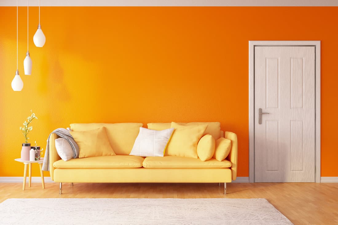 Interior of an orange painted living room with a long orange sofra and white dangling lamps