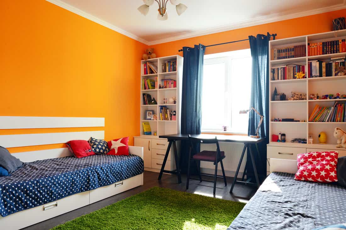 Interior of an orange themed bedroom with orange colored walls and blue beddings