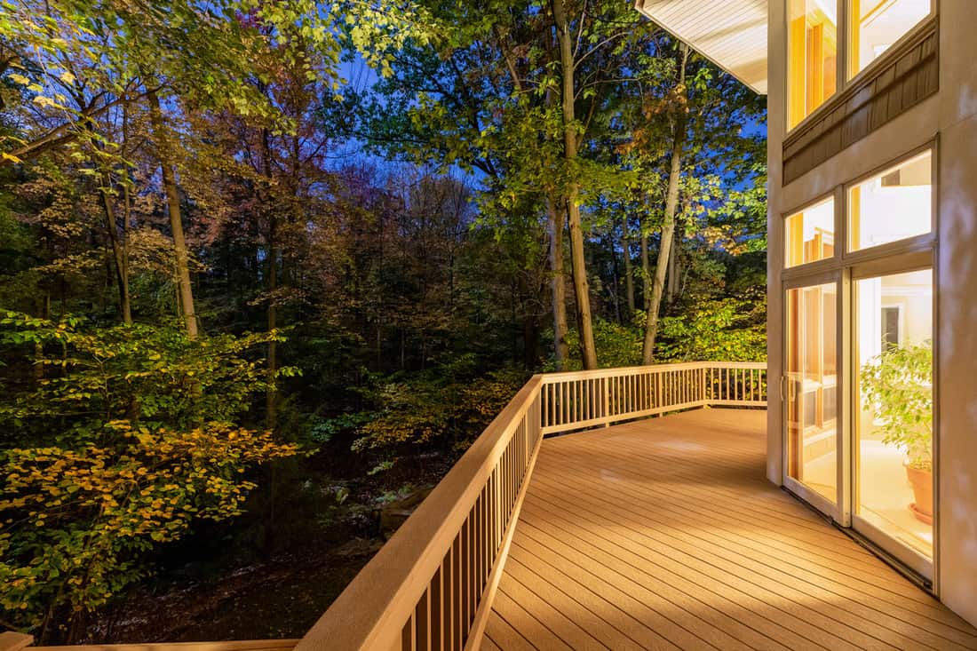 Large composite deck on a luxury home in the woods photographed at night. Concepts could include architecture, design, outdoor living, luxury living, nature, others.