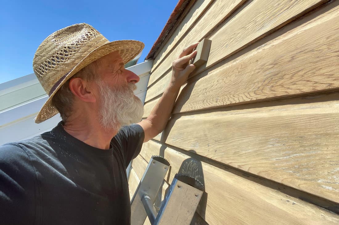 Man is sanding a wooden wall for home maintenance
