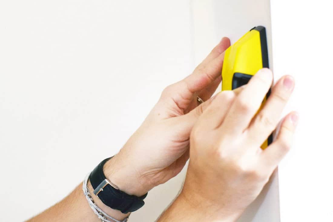 Man using stud finder to search apartment wall for studs