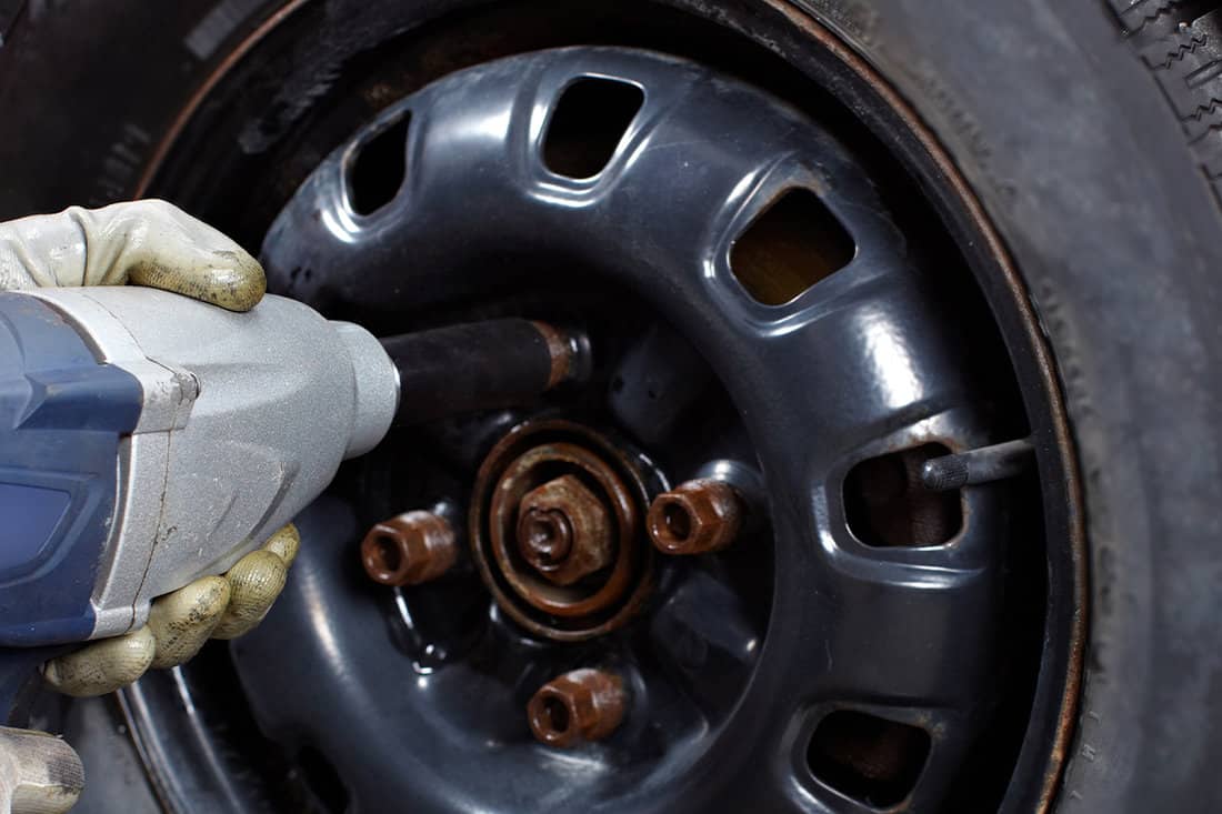 Mechanic removing stud on car wheel with impact wrench