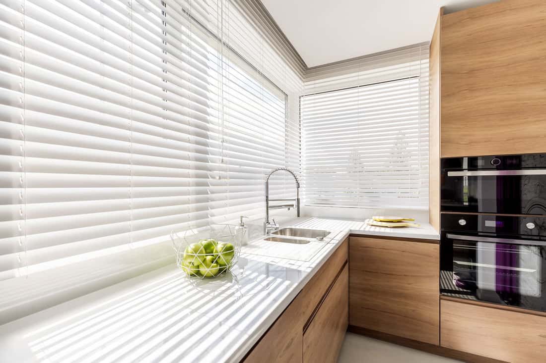 Modern bright kitchen interior with white horizontal window blinds, wooden cabinets