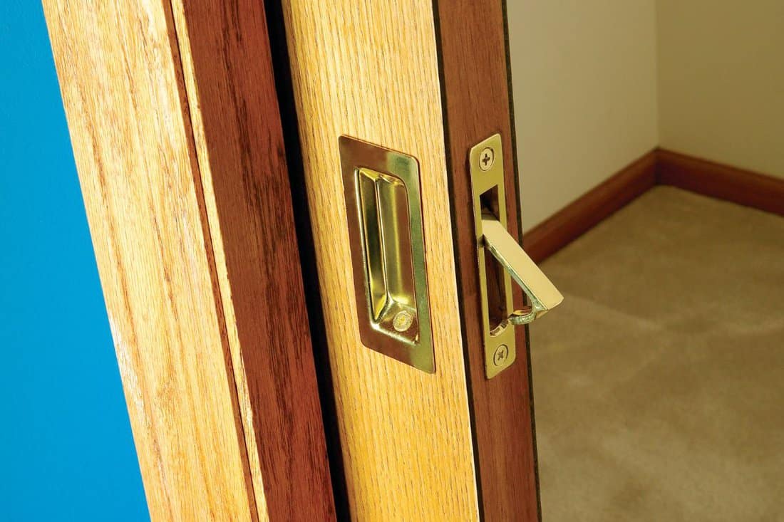 Open wooden pocket door slid back into the wall cavity concealing it and saving space with close up focus to the handle and pull edge lever