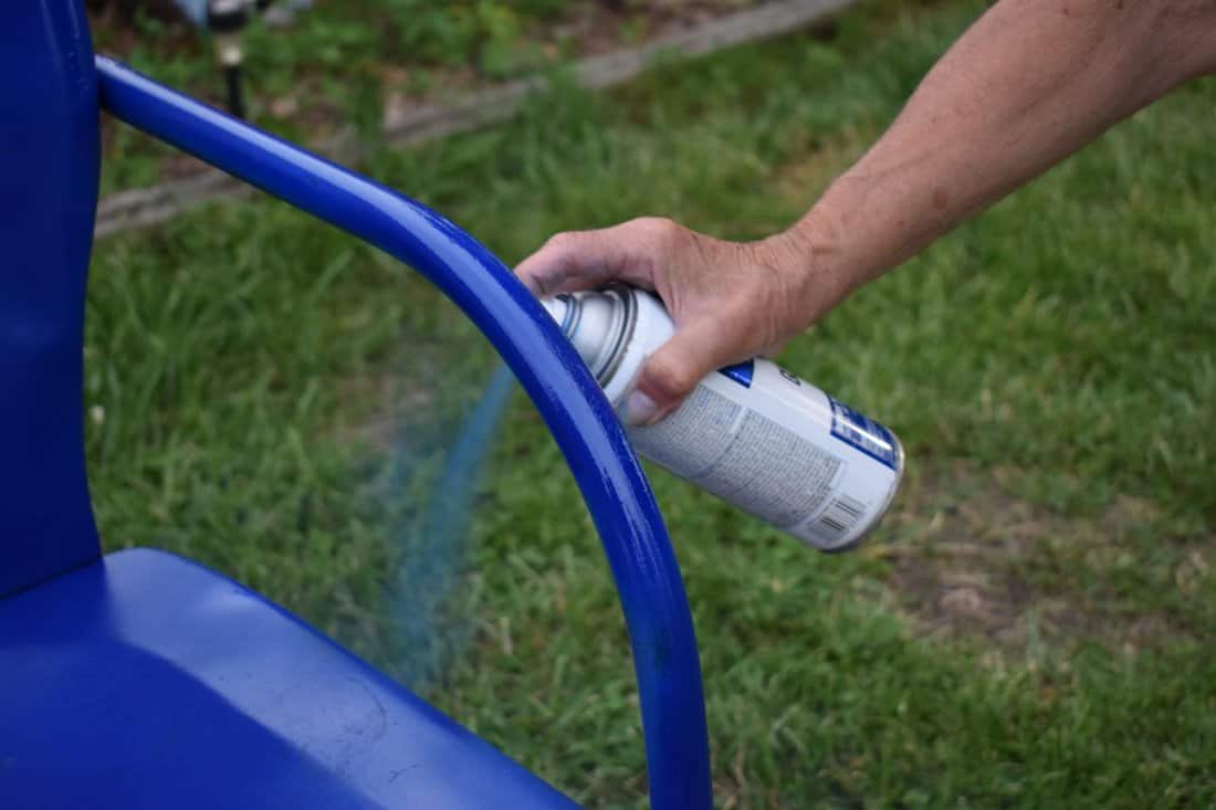 Person spray painting a metal lawn chair